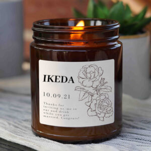 Dark brown glass jar woody scented candle for office use, with branded label, shown lit.